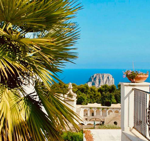 Balcon avec palmier à Capri offrant une vue sur la mer Méditerranée et les rochers Faraglioni.