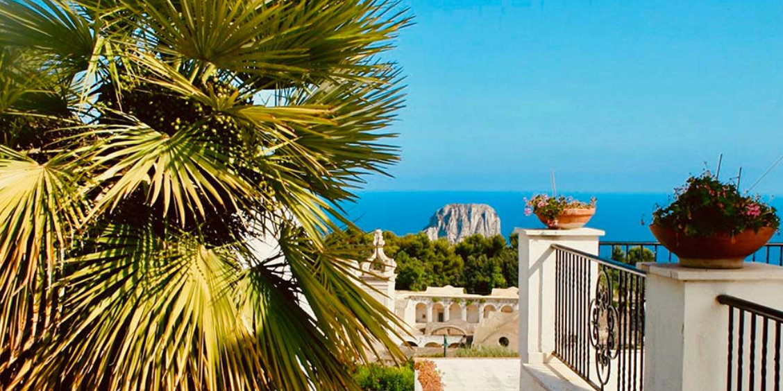 Balcon avec palmier à Capri offrant une vue sur la mer Méditerranée et les rochers Faraglioni.