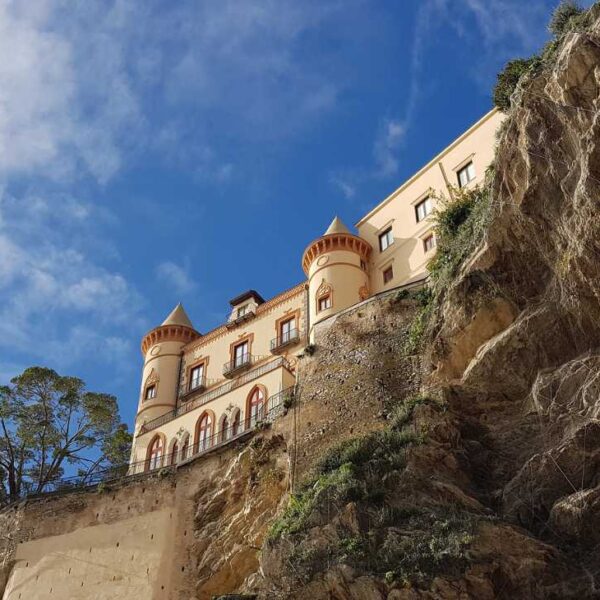 Palais perché sur une falaise à Maiori, entre roche, ciel bleu et paysage de la Côte Amalfitaine.
