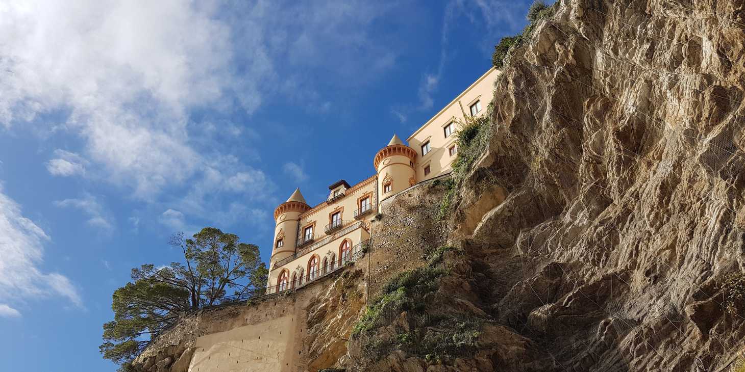 Palais perché sur une falaise à Maiori, entre roche, ciel bleu et paysage de la Côte Amalfitaine.