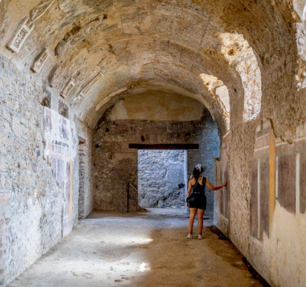 Galerie voûtée de la Maison du Cryptoportique à Pompéi avec des restes de fresques et une personne observant les murs.