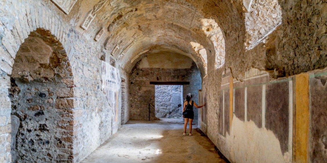 Galerie voûtée de la Maison du Cryptoportique à Pompéi avec des restes de fresques et une personne observant les murs.