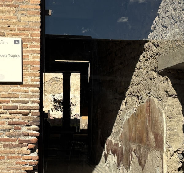 Entrée de la Maison du Poète tragique à Pompéi, montrant un mur de briques antiques et une plaque informative.