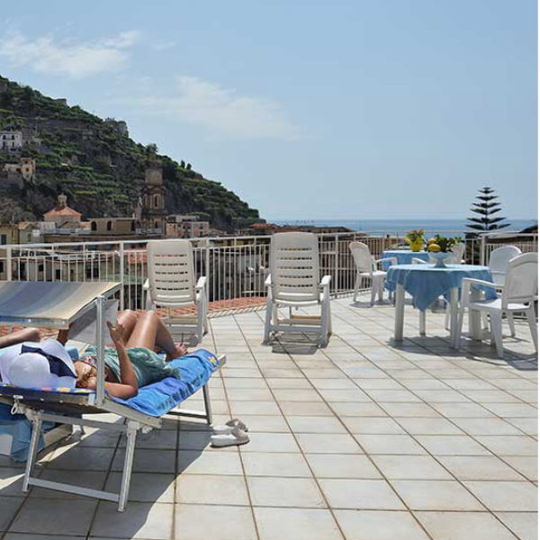 Grande terrasse solarium de la Maison Raphael avec transats et vue panoramique sur Minori et la mer.