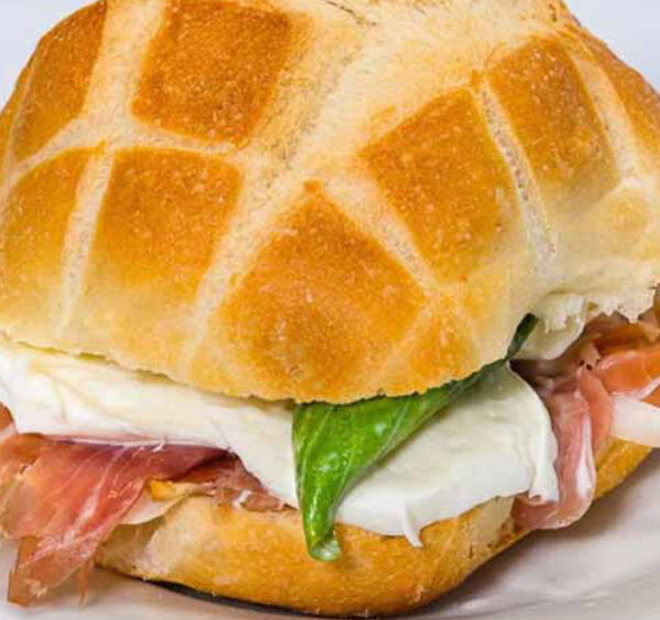 Sandwich italien avec mozzarella, jambon cru et basilic servi sur une assiette.