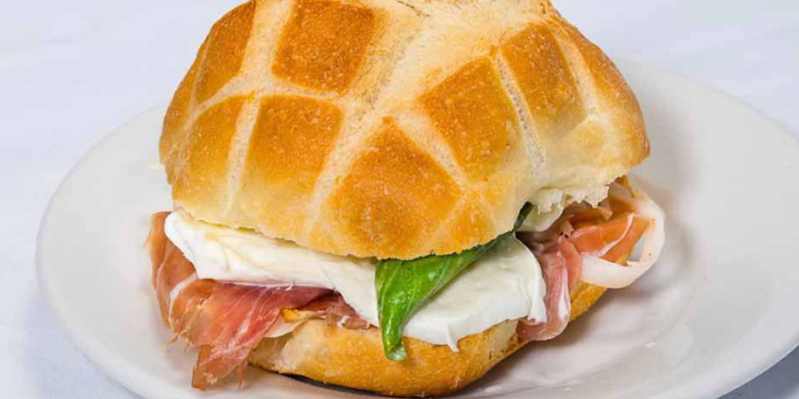 Sandwich italien avec mozzarella, jambon cru et basilic servi sur une assiette.