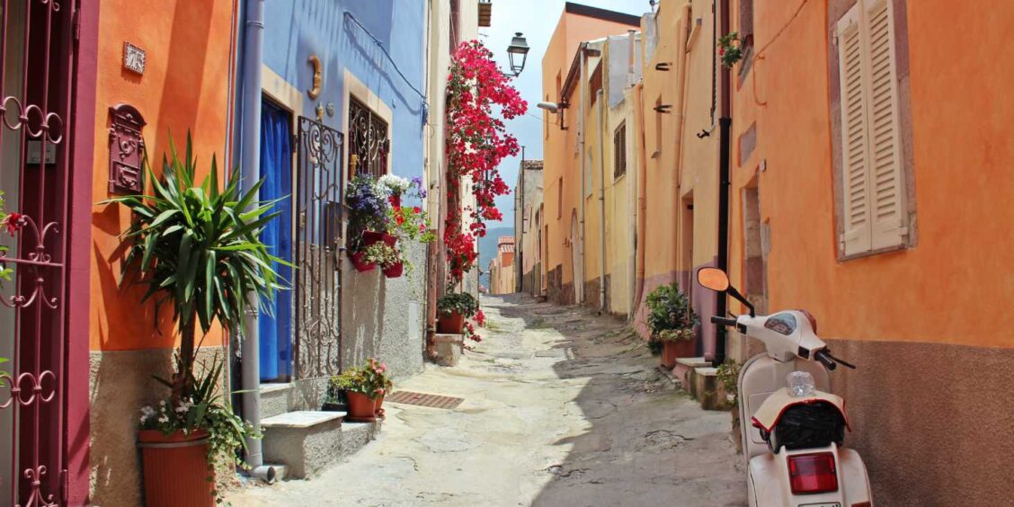 Ruelle typique de Marina Chiaiolella à Procida, Campanie, ornée de fleurs et d'un scooter blanc traditionnel.