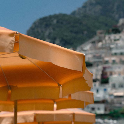 Gros plan sur des parasols orange typiques de la plage Marina Grande avec le village de Positano en arrière-plan.