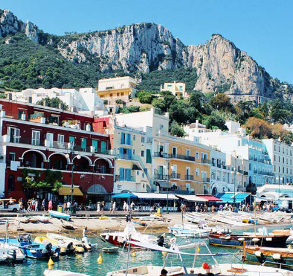 Maisons colorées et nombreux bateaux au port de Marina Grande à Capri au pied de hautes falaises rocheuses.