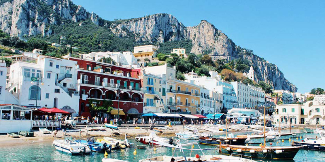 Maisons colorées et nombreux bateaux au port de Marina Grande à Capri au pied de hautes falaises rocheuses.