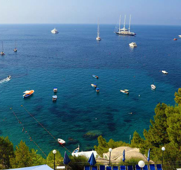 Vue surplombant la baie de Marina Piccola à Capri avec de nombreux bateaux sur des eaux turquoise et des falaises escarpées.
