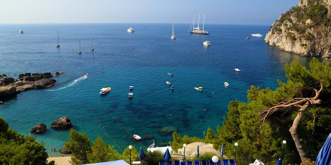 Vue surplombant la baie de Marina Piccola à Capri avec de nombreux bateaux sur des eaux turquoise et des falaises escarpées.