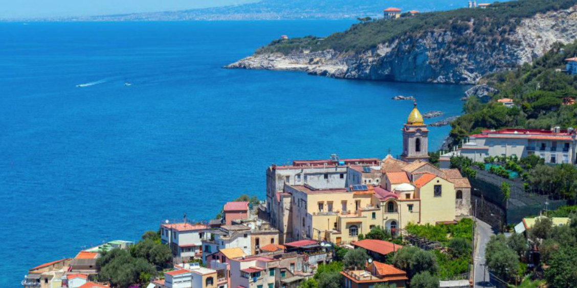 Massa Lubrense vue depuis la côte avec église, maisons et mer bleue.