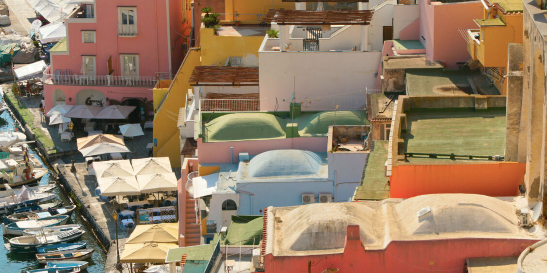 Gros plan sur les maisons colorées de Marina Corricella à Procida, Campanie, avec ses bateaux amarrés et parasols de quai.