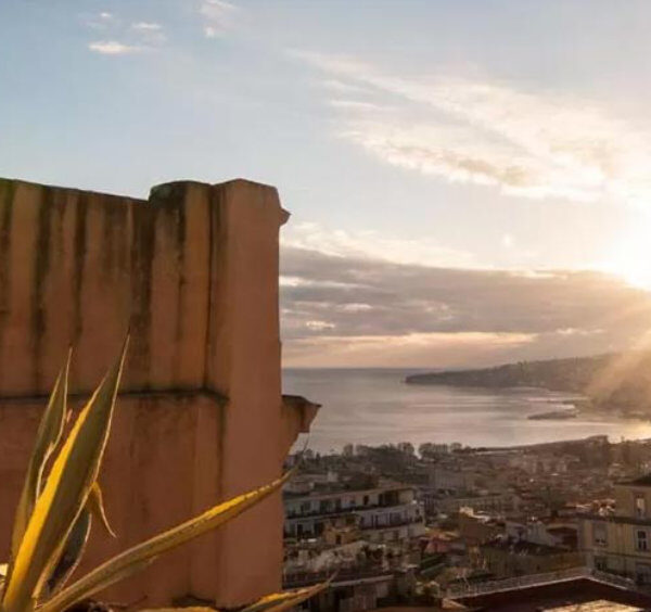 Vue panoramique sur Naples au coucher du soleil avec le golfe et les toits de la ville depuis une chambre d’hôtes.