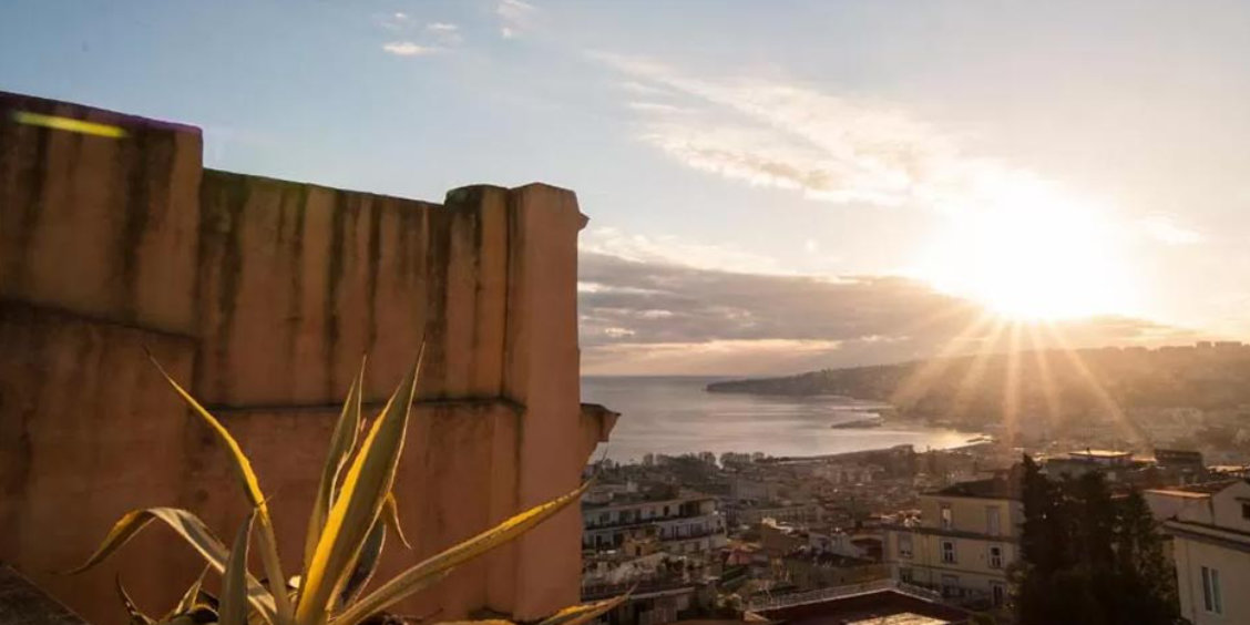Vue panoramique sur Naples au coucher du soleil avec le golfe et les toits de la ville depuis une chambre d’hôtes.