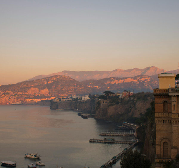 Sorrente au coucher du soleil avec hôtels sur les falaises, mer calme et côte illuminée.