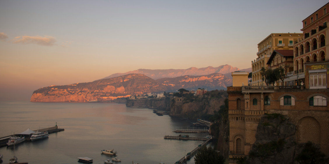 Sorrente au coucher du soleil avec hôtels sur les falaises, mer calme et côte illuminée.