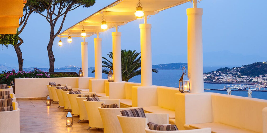 Terrasse illuminée du San Montano Resort & Spa offrant une vue romantique sur la baie au crépuscule.