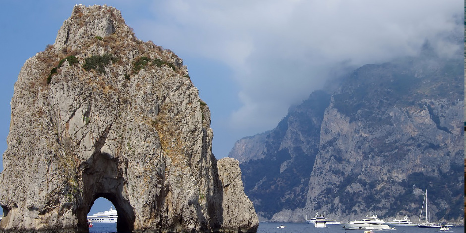 Rocher Faraglione avec son arche naturelle au premier plan et montagnes brumeuses en arrière-plan à Capri.