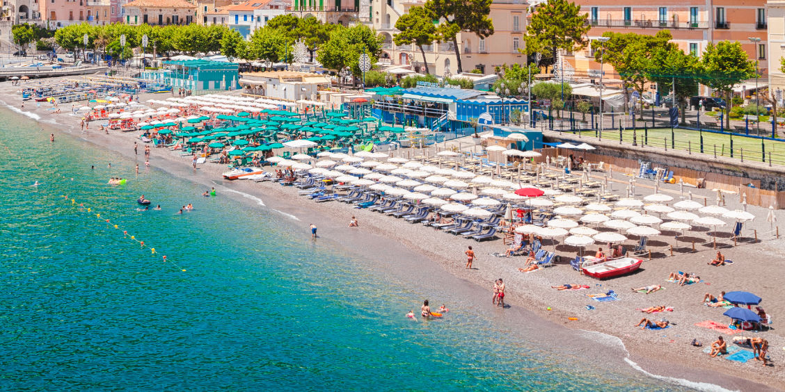 Grande plage de Minori avec ses rangées de parasols verts et blancs.