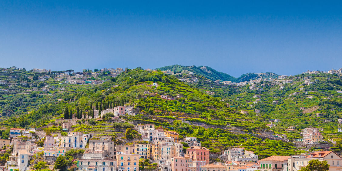 Maisons de Minori et jardins en terrasses à flanc de colline sous un ciel bleu.