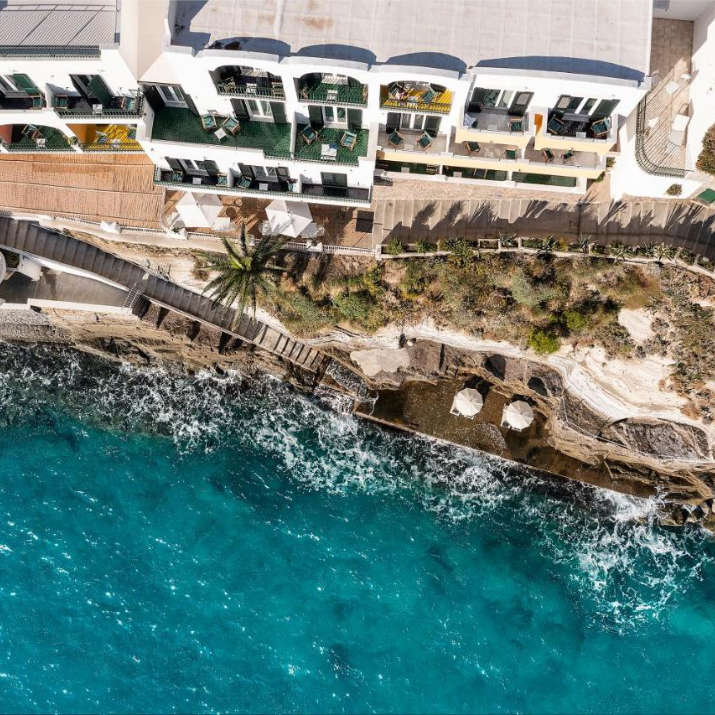 Vue aérienne spectaculaire du Miramare Sea Resort & Spa construit à flanc de falaise au-dessus d'eaux turquoise.