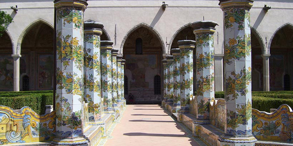 Cloître du monastère de Santa Chiara à Naples avec colonnes décorées de majoliques colorées et jardin intérieur.
