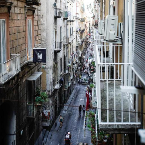 Rue typique de Naples vue depuis un balcon avec façades anciennes et vie urbaine animée.
