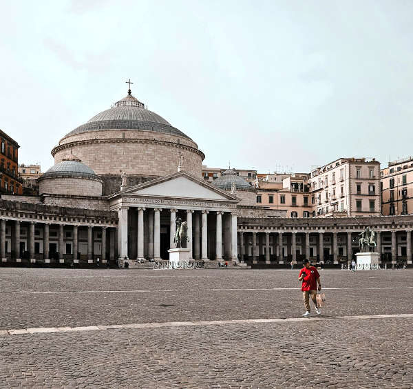 Vue panoramique de la place du Plebiscito à Naples avec la basilique San Francesco di Paola et sa colonnade sous un ciel clair.