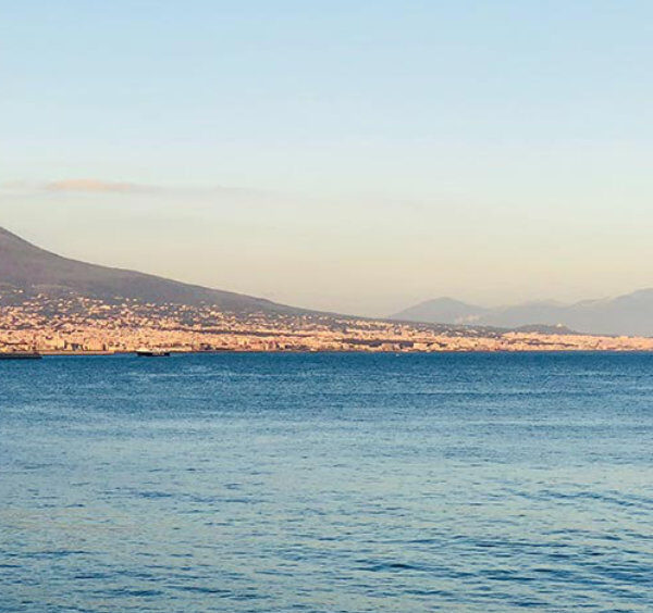 Vue panoramique sur la mer Méditerranée avec le mont Vésuve et la ville de Naples au coucher du soleil, un voilier seul sur l'eau.