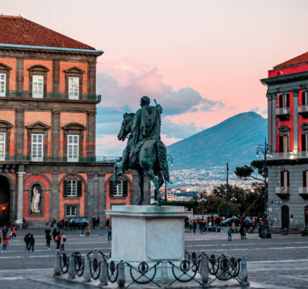 Place du Plébiscite à Naples avec statue équestre et vue sur le Vésuve au coucher du soleil.