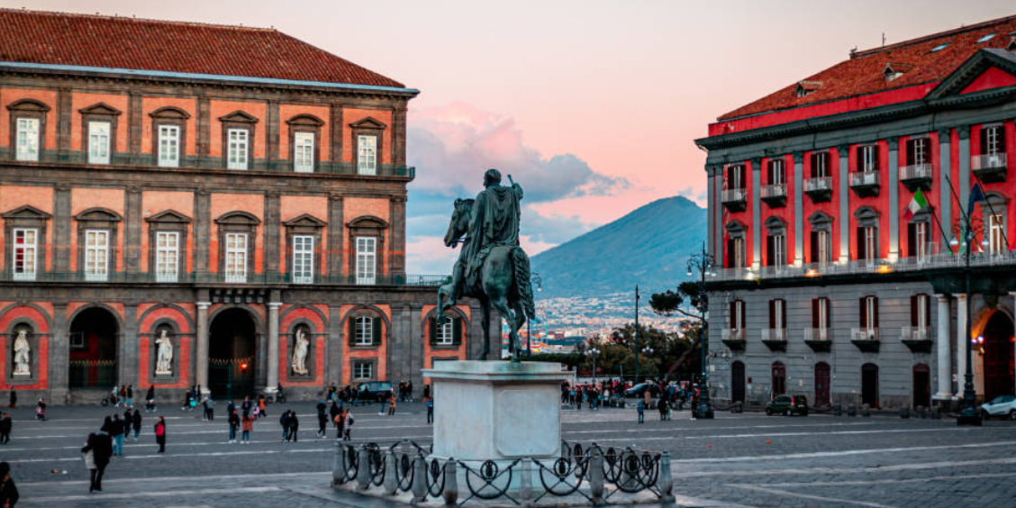 Place du Plébiscite à Naples avec statue équestre et vue sur le Vésuve au coucher du soleil.