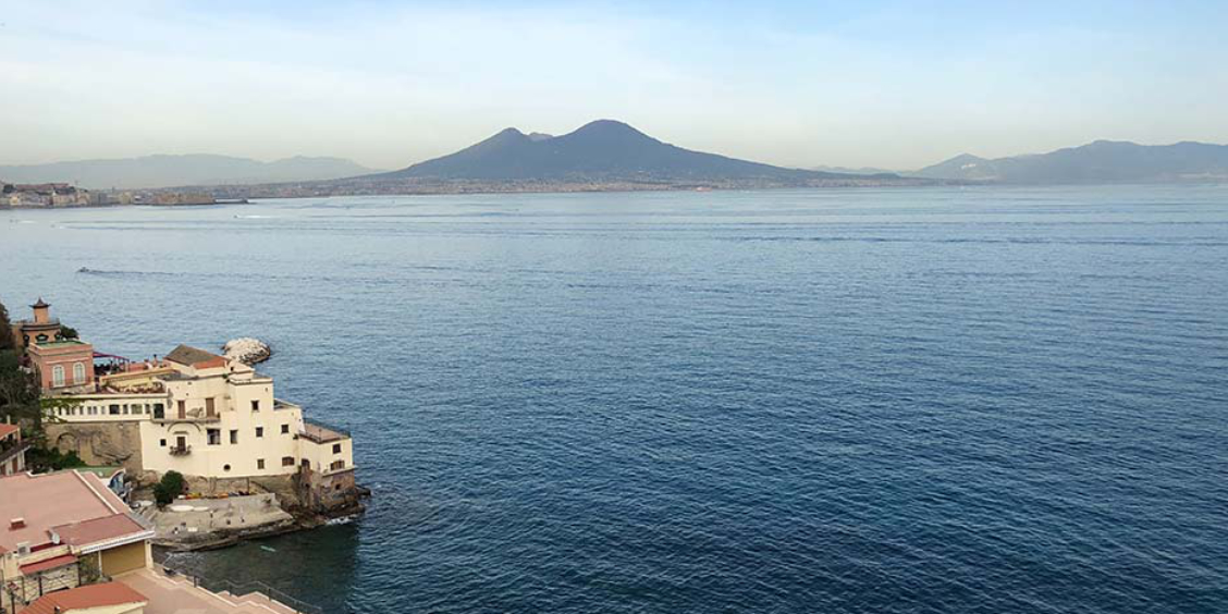 Vue panoramique du golfe de Naples avec le Vésuve en arrière-plan et la côte napolitaine au premier plan.