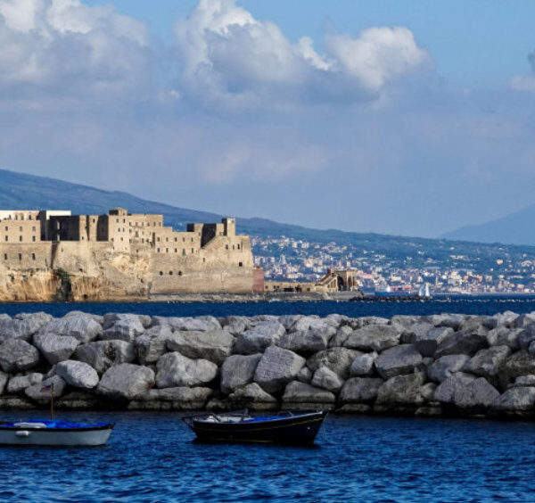 Le Castel dell'Ovo à Naples vu depuis la mer avec des barques et une digue en juin.