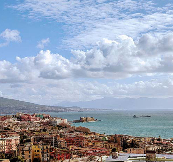 Vue panoramique de Naples avec le Vésuve et le golfe sous un ciel printanier.