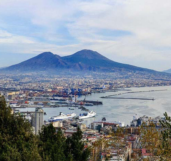 Vue panoramique de Naples, avec le Vésuve et son port rempli de navires de croisière.