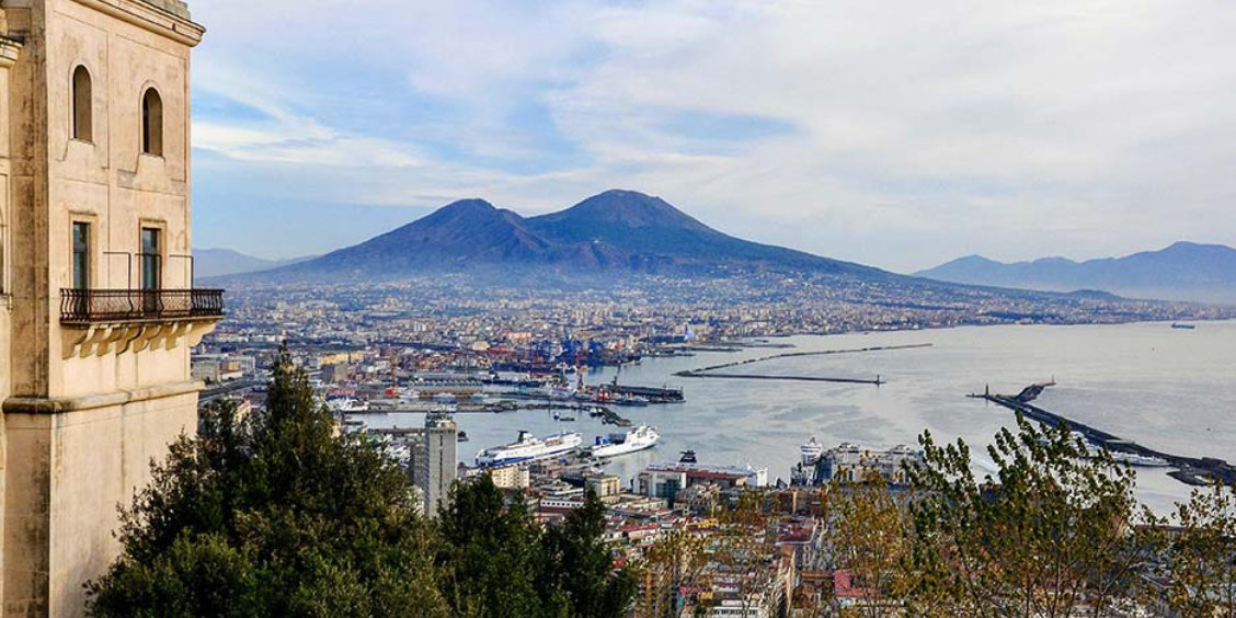 Vue panoramique de Naples, avec le Vésuve et son port rempli de navires de croisière.
