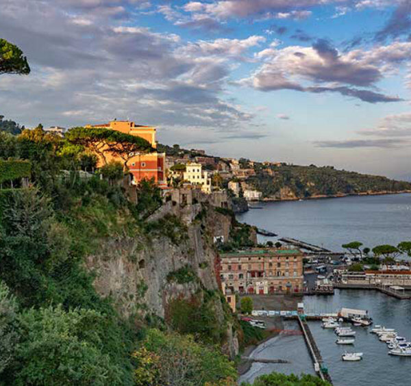 Sorrente en novembre avec port, falaises verdoyantes et ciel nuageux au coucher du soleil.