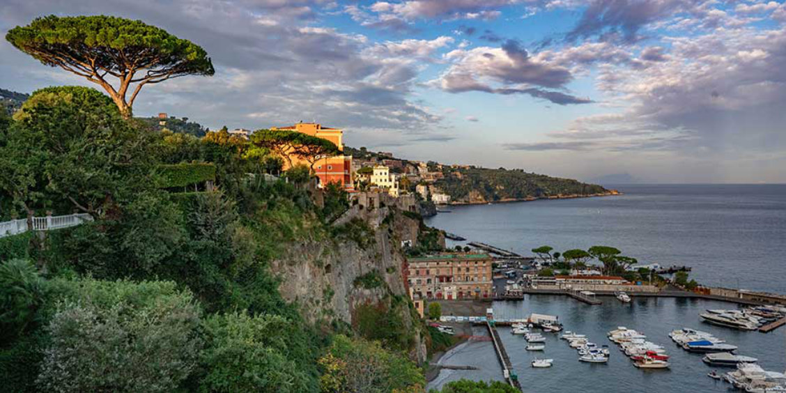 Sorrente en novembre avec port, falaises verdoyantes et ciel nuageux au coucher du soleil.