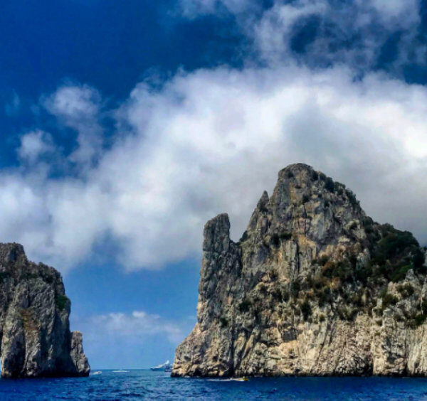 Les imposants rochers Faraglioni à Capri émergeant de la mer bleue sous un ciel chargé de gros nuages blancs en octobre.