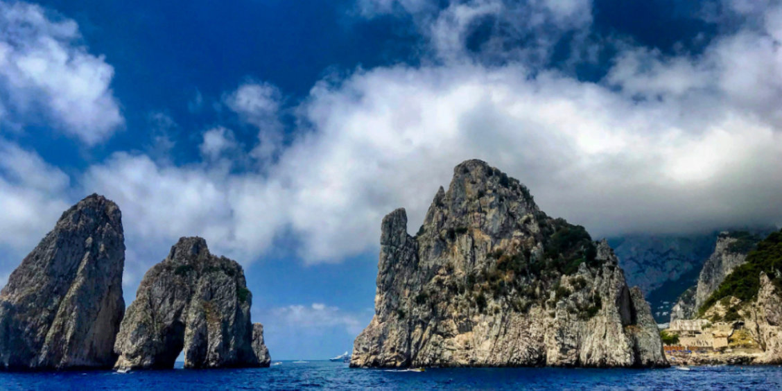 Les imposants rochers Faraglioni à Capri émergeant de la mer bleue sous un ciel chargé de gros nuages blancs en octobre.