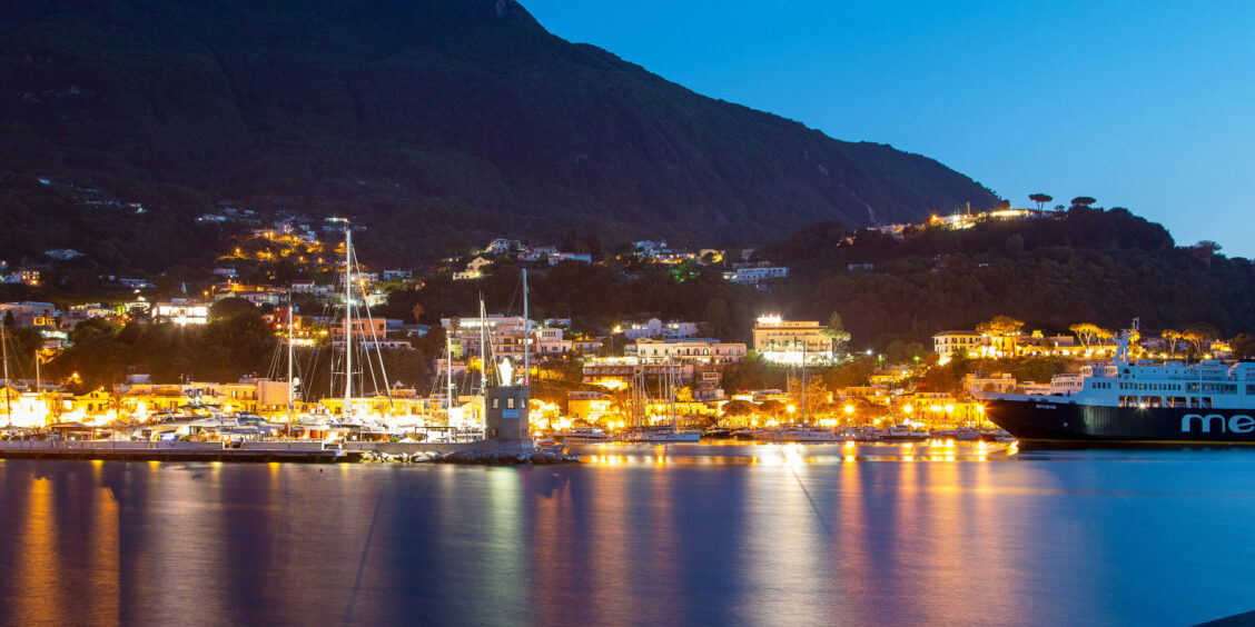Vue nocturne du port d'Ischia illuminé avec les reflets des lumières sur l'eau.