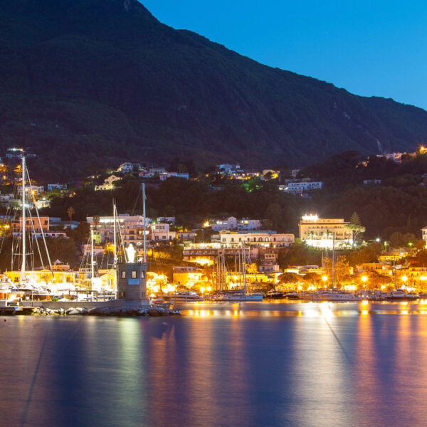 Vue nocturne du port d'Ischia illuminé avec les reflets des lumières sur l'eau.
