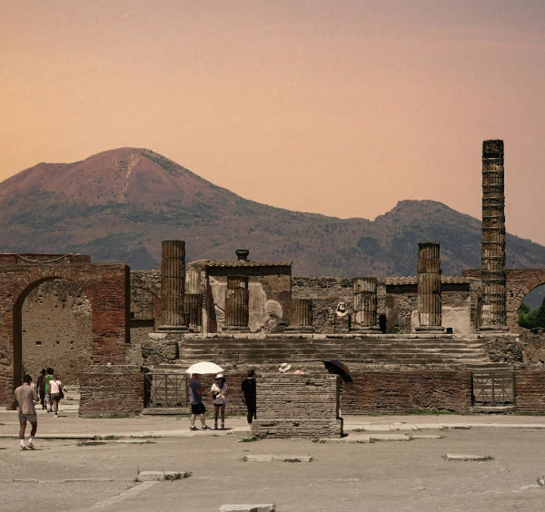 Vue panoramique des ruines du forum de Pompéi avec le mont Vésuve en arrière-plan sous un ciel orangé.