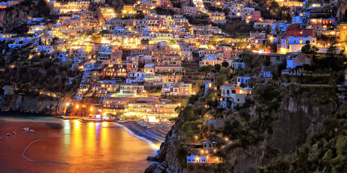 Positano illuminé le soir avec ses maisons sur la falaise et la baie de la Côte Amalfitaine.