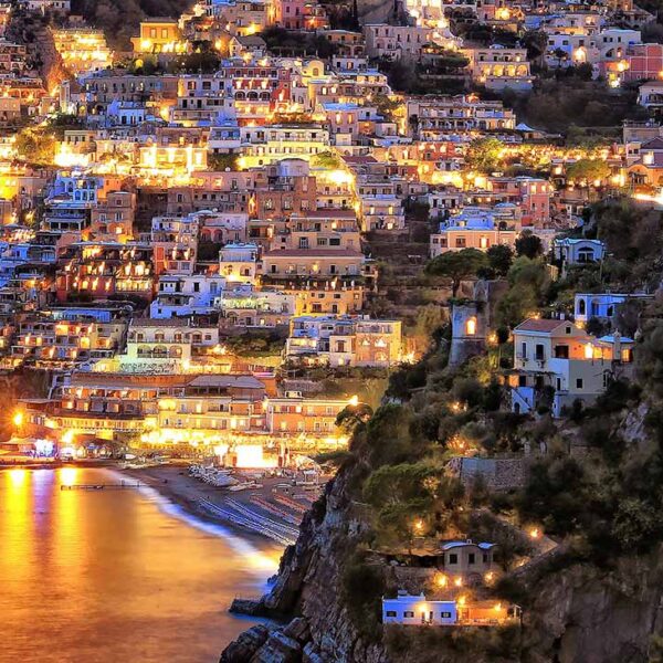 Positano illuminé le soir avec ses maisons sur la falaise et la baie de la Côte Amalfitaine.