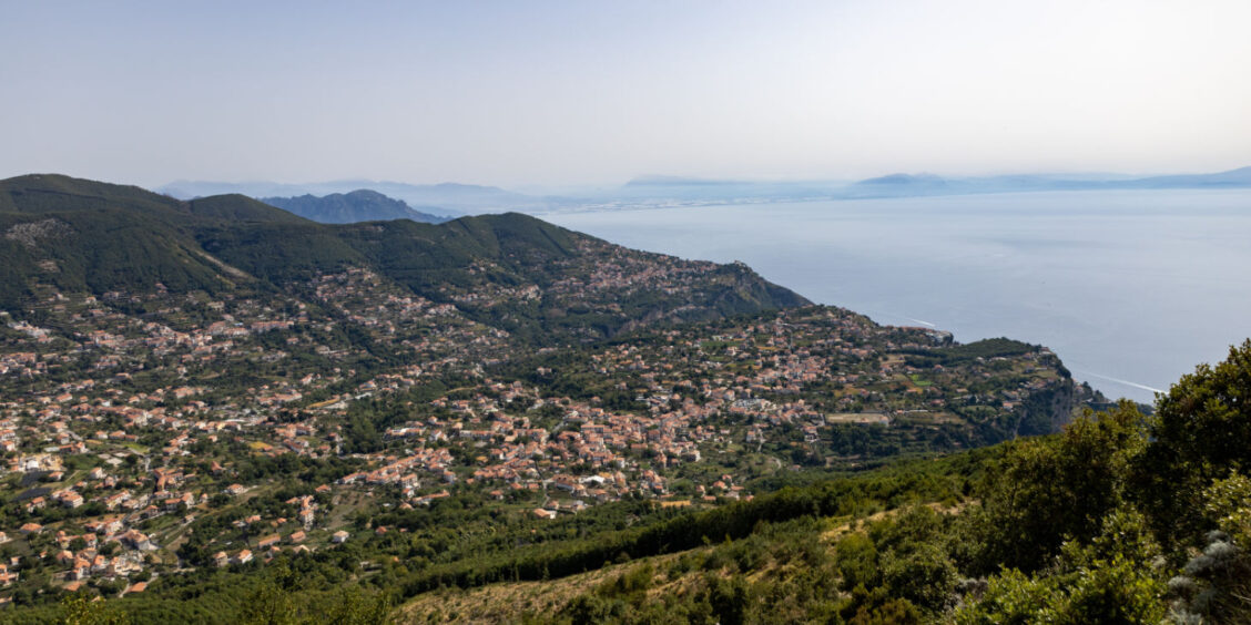 Vue panoramique sur Agerola et la Côte Amalfitaine entre montagnes verdoyantes et mer en arrière-plan.