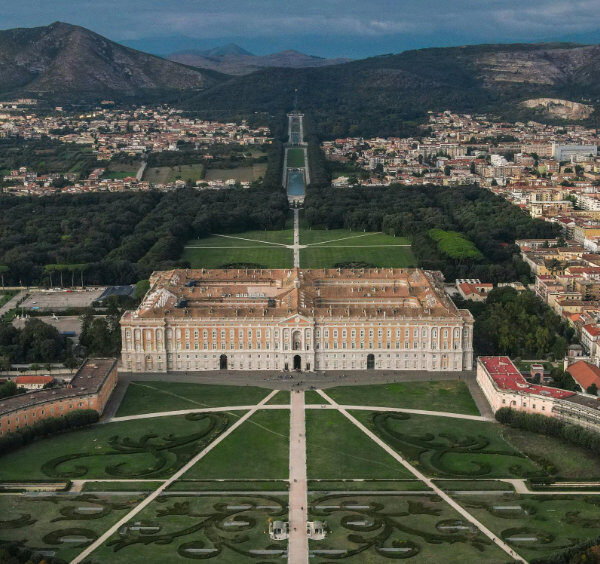 Palais royal de Caserte vu du ciel avec jardins symétriques, parc et ville en arrière-plan.