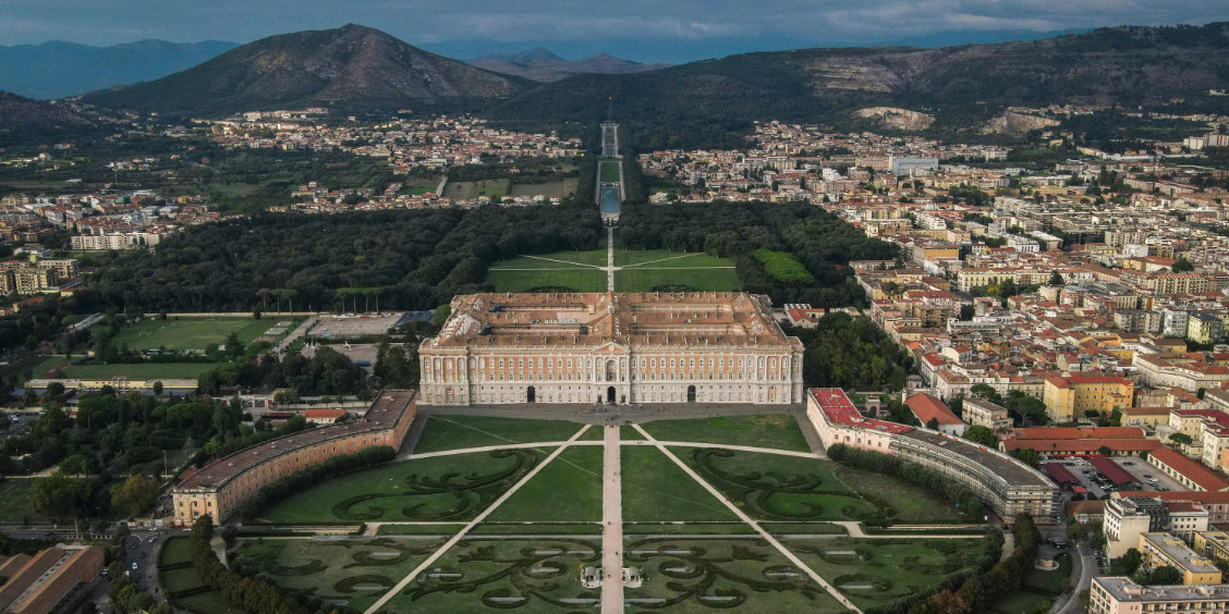 Palais royal de Caserte vu du ciel avec jardins symétriques, parc et ville en arrière-plan.